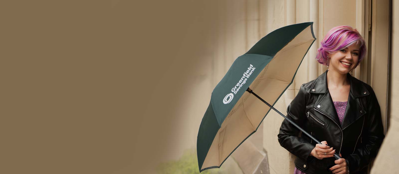 photo of a smiling woman holding a green umbrella with the Greenfield Savings Bank logo on it.
